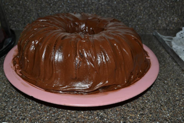Chocolate bundt cake with glossy frosting on a pink plate, warm brown tones