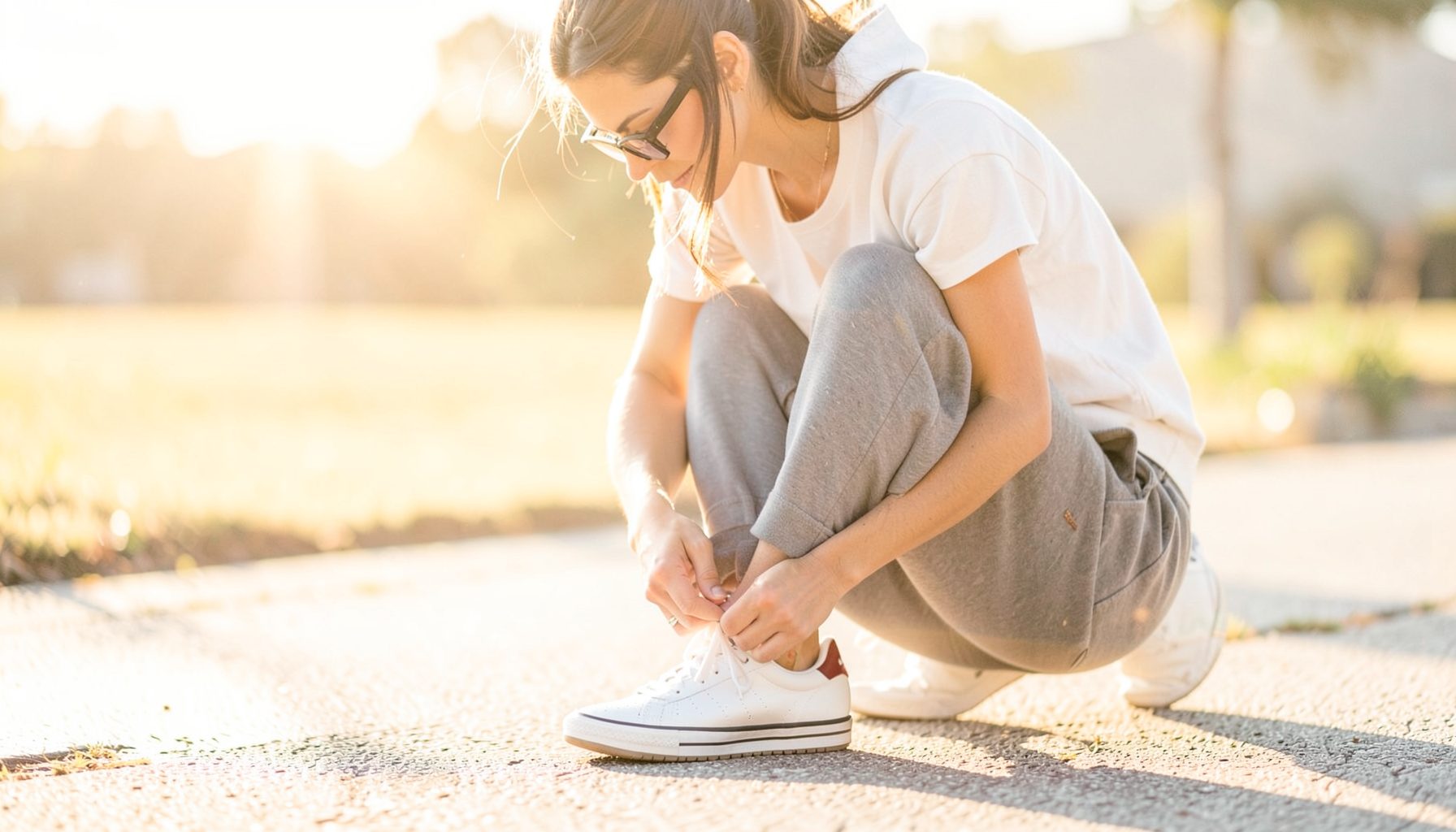 Woman lacing up sneakers on a sunlit morning, soft golden and white tones